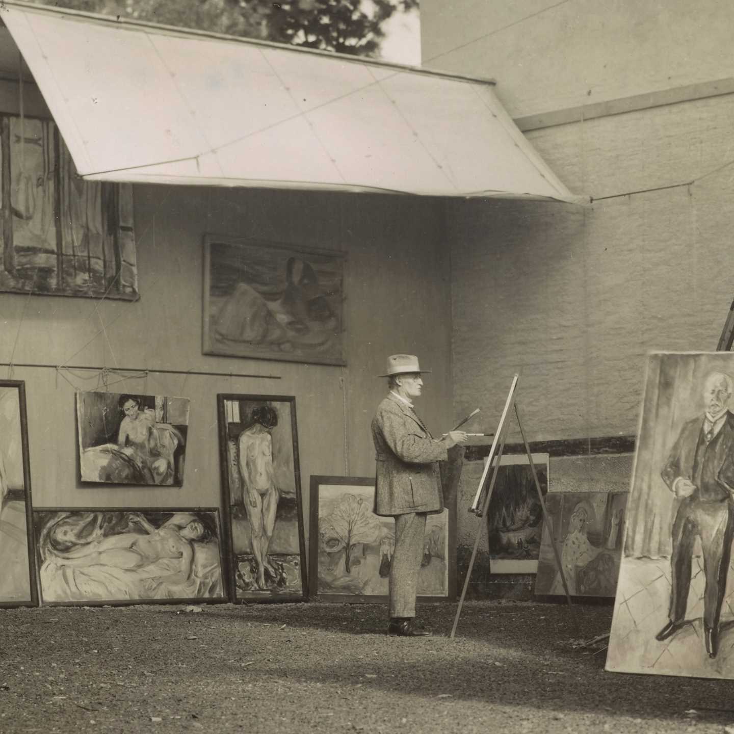 Edvard Munch is standing and painting in his open-air studio at Ekely. He is surrounded by his own works and is wearing a hat to shield himself from the sun and a light-coloured suit.