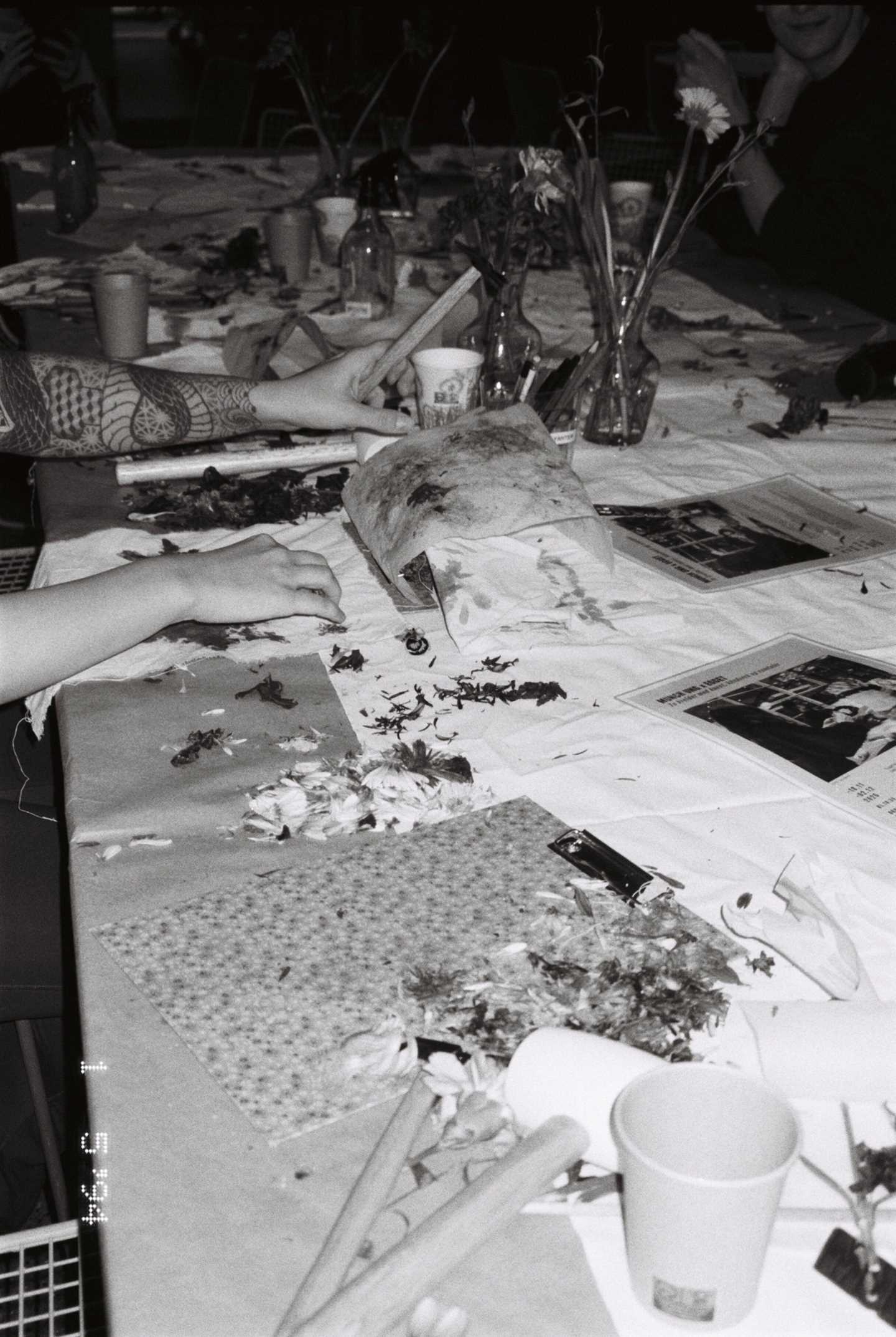 A workshop table where several people are seated, making handicrafts. Photograph.