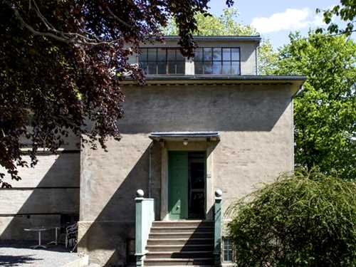 The winter studio at Ekely seen from the outside. A grey stone building with steps leading up to a green entrance door.