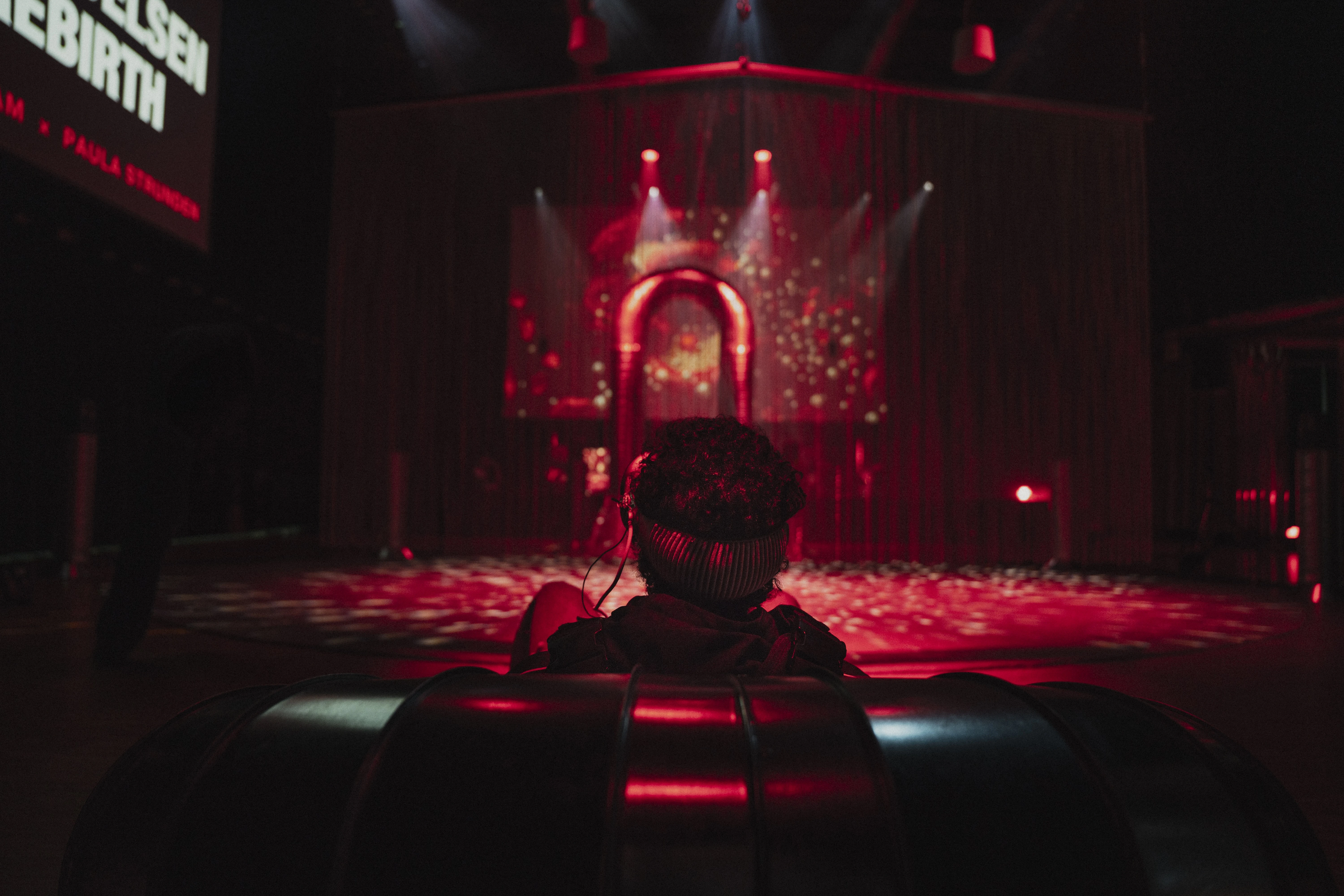 A boy sits with his back to the camera wearing VR goggles. He is looking towards a portal illuminated in red light. Photograph.