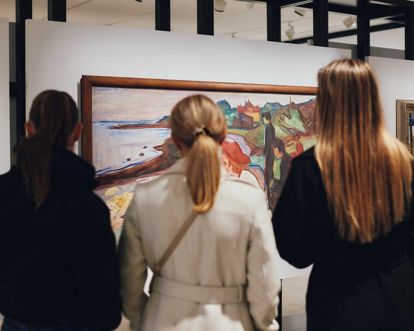 Three women with their backs to the camera looking at a painting by Edvard Munch. Photograph.