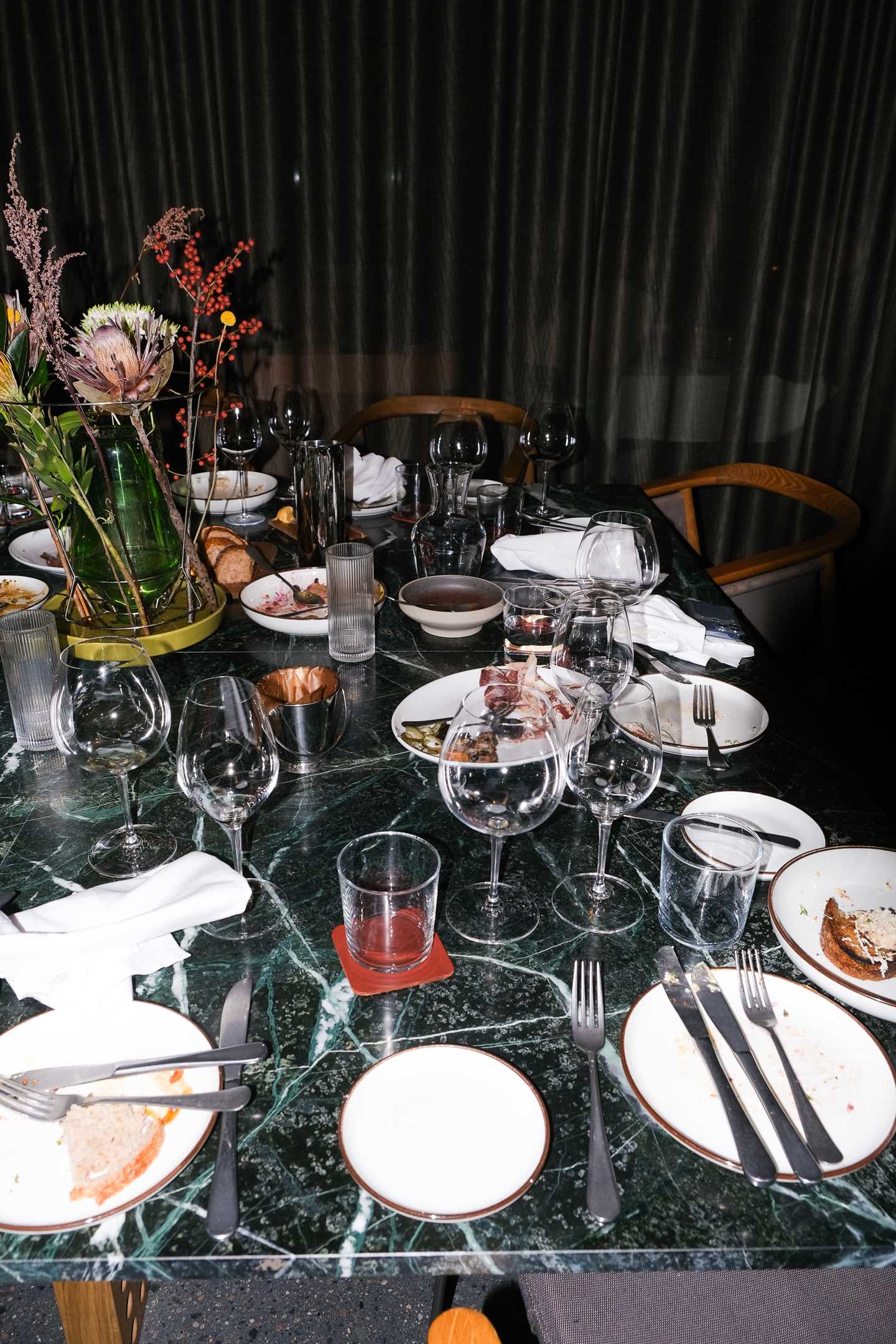 An abandoned restaurant table with used glasses and plates, along with discarded napkins and chairs pushed away from the table. Photograph.