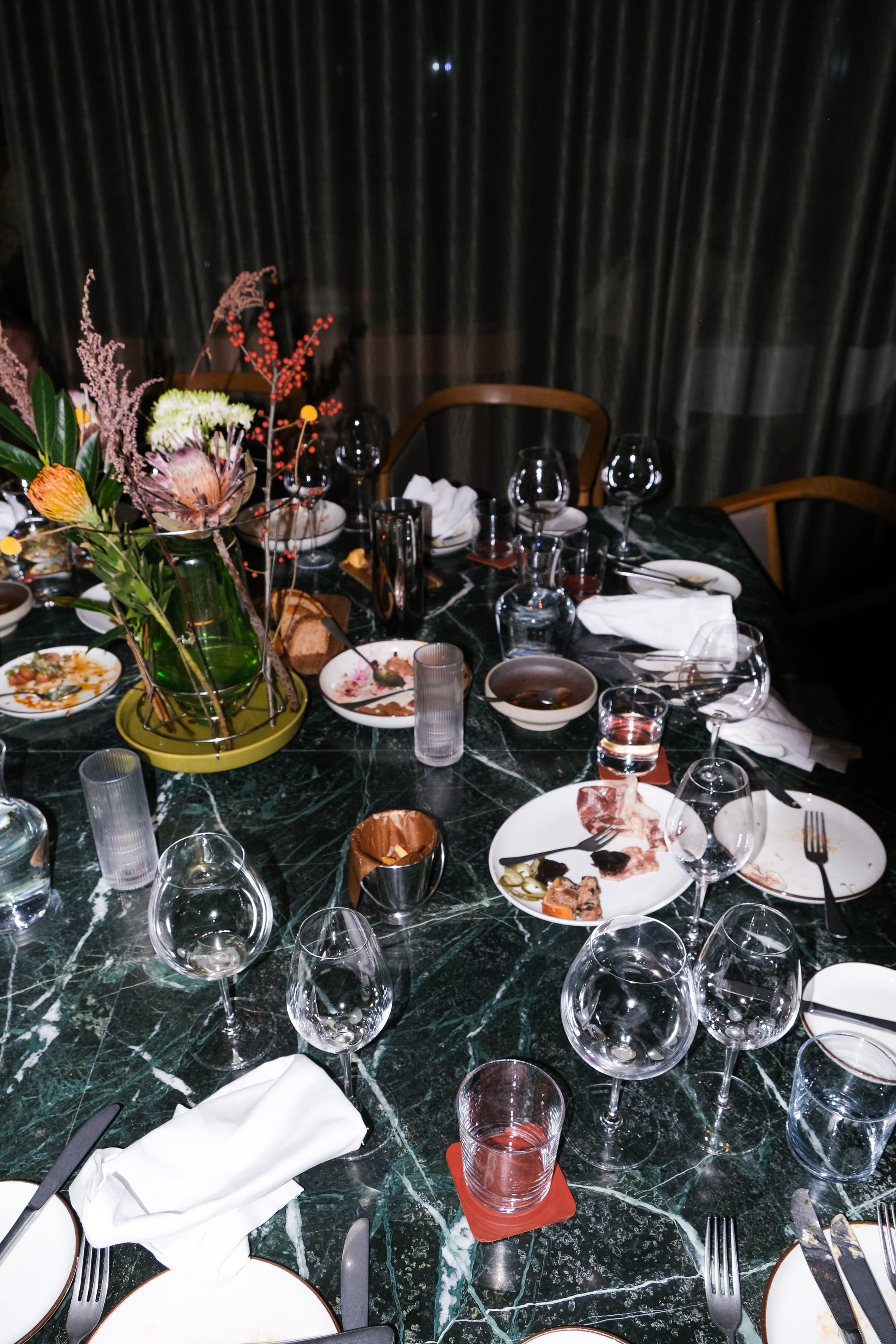 An abandoned restaurant table with used glasses and plates, along with discarded napkins and chairs pushed away from the table. Photograph.