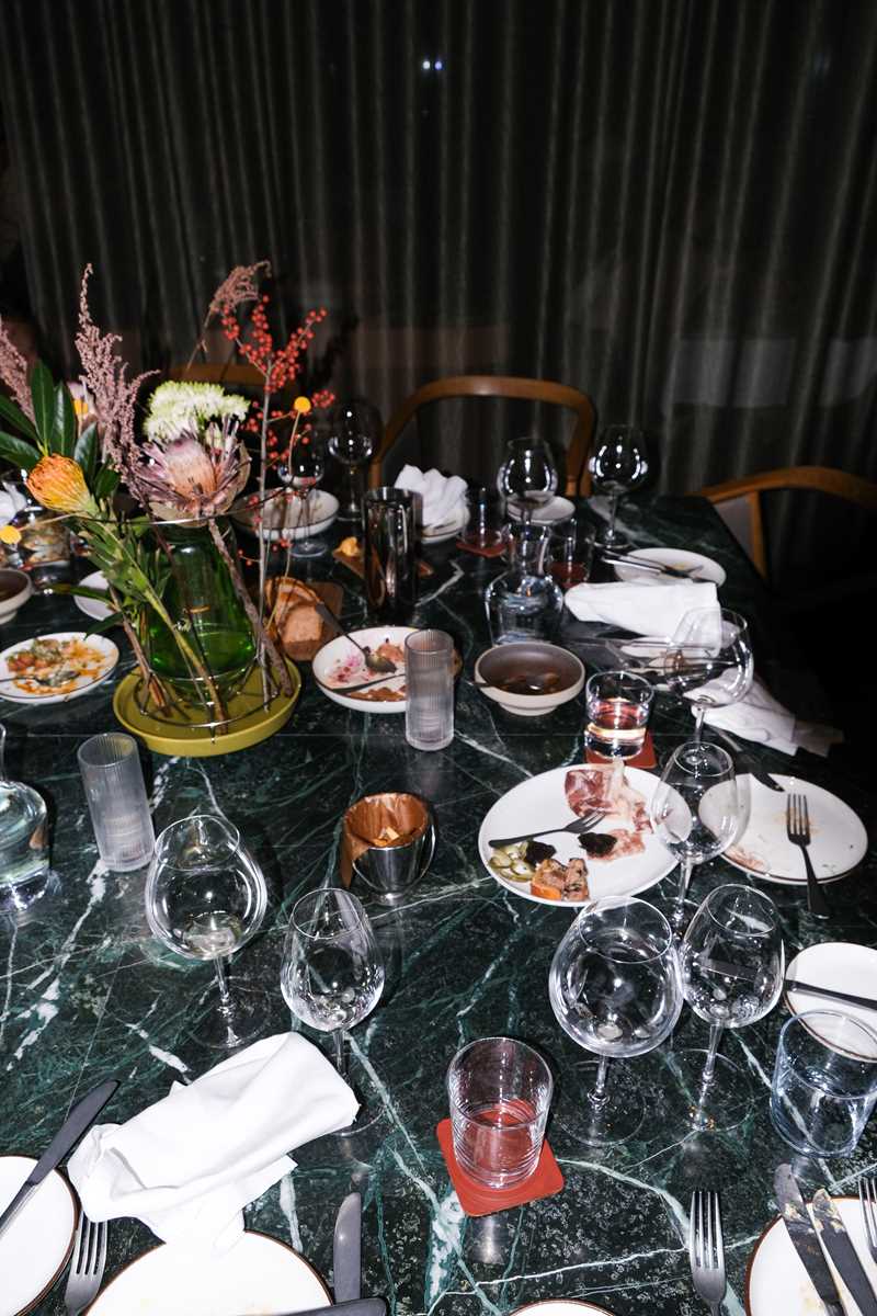An abandoned restaurant table with used glasses and plates, along with discarded napkins and chairs pushed away from the table. Photograph.