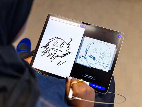 A woman is drawing on a tablet and is shown a similar drawing made by Edvard Munch. Photograph.