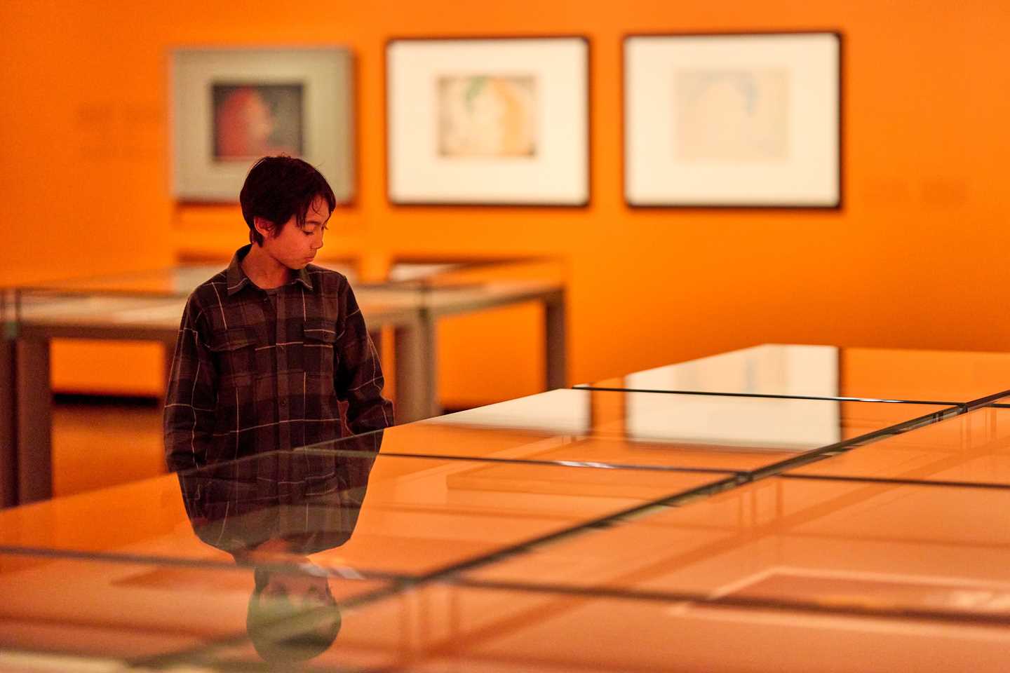 A young boy standing by a glass case looking at prints by Edvard Munch in the Inntil exhibition. Photograph.