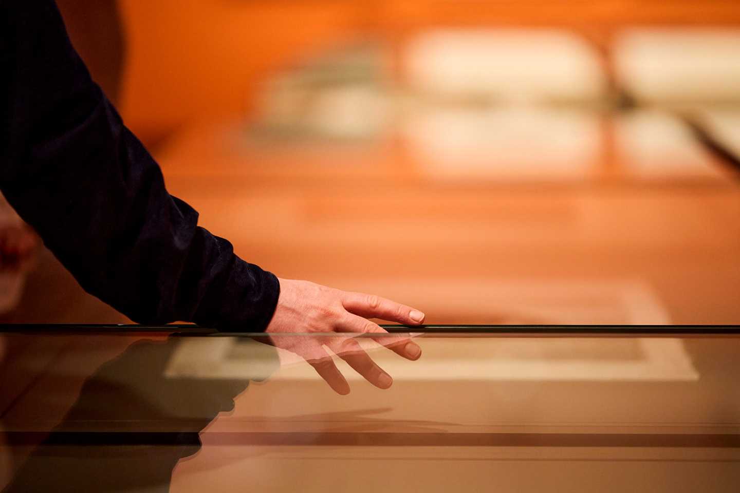Close-up of a hand touching a glass case. Photograph.