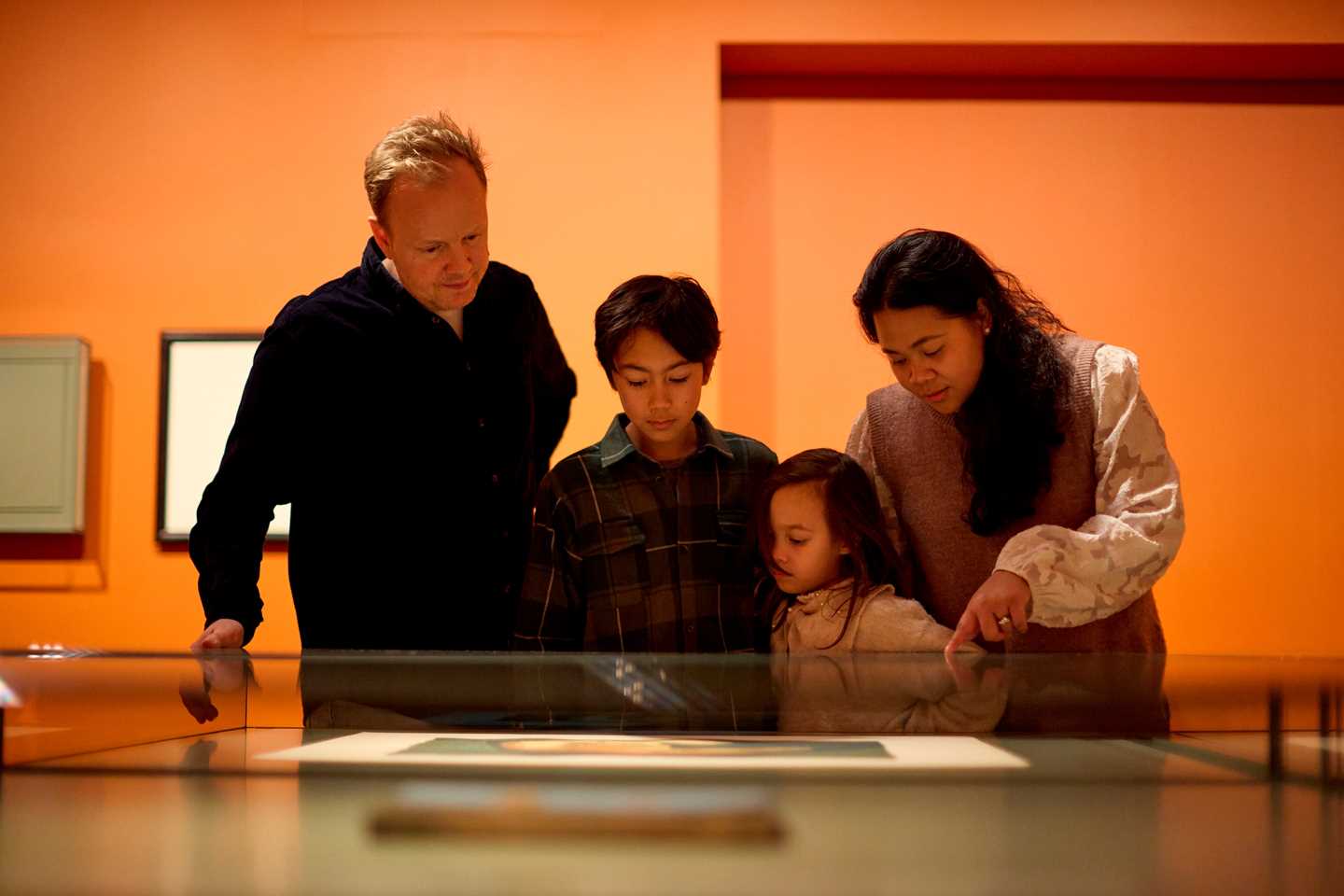A family of four looking at a graphic print by Edvard Munch in a glass case. Photograph.