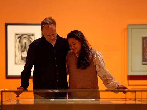 A couple embracing while looking at a glass case with prints by Edvard Munch. Photograph.