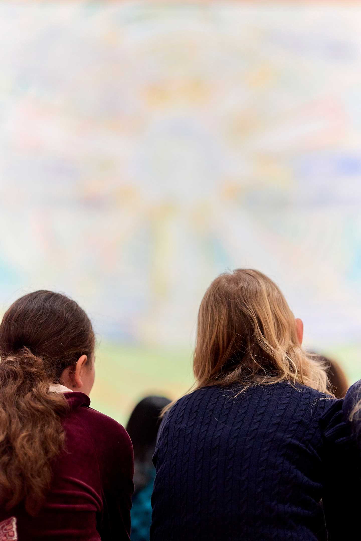 Two girls sit with their backs to the camera, looking at The Sun by Edvard Munch. Photograph.