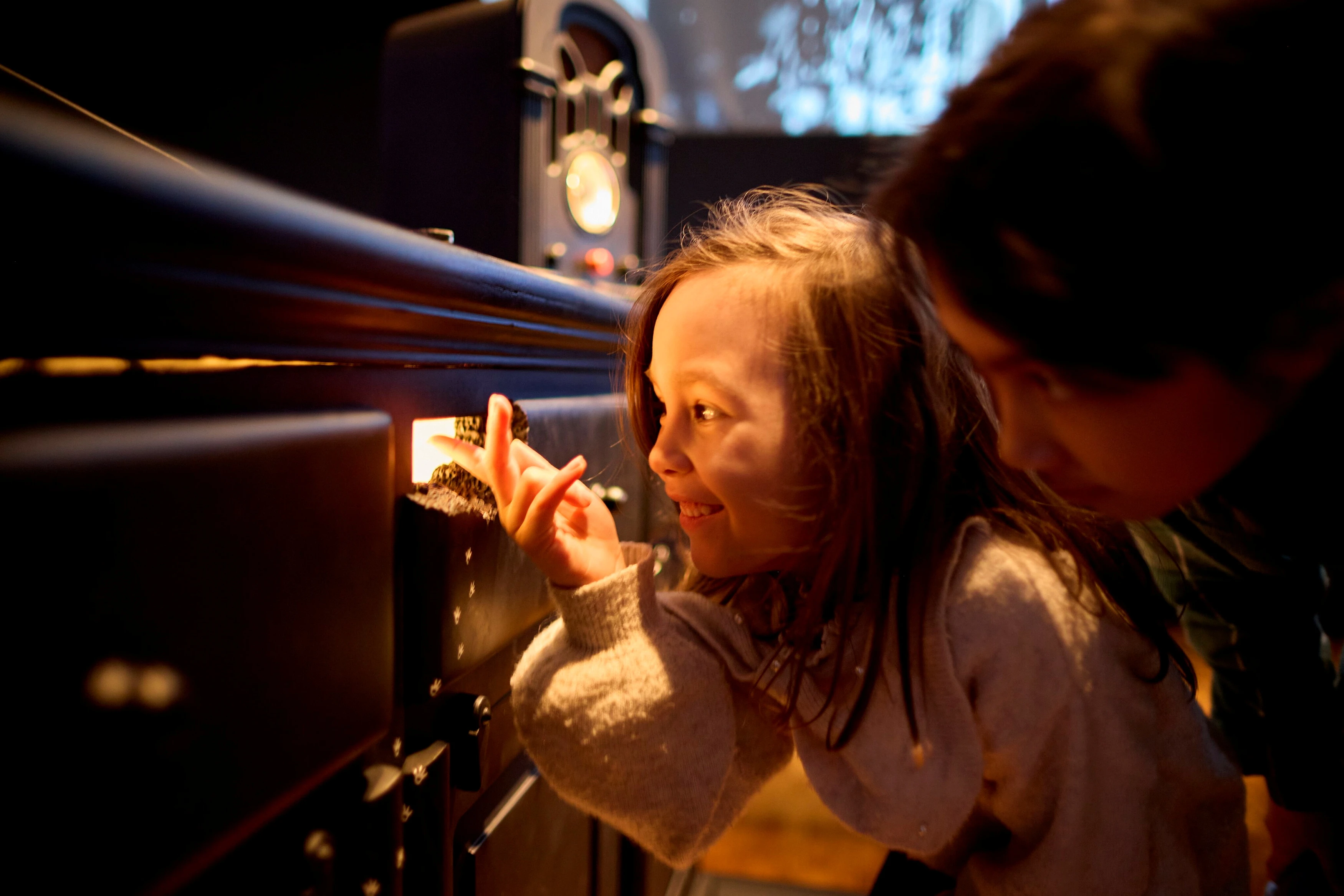 Two children crouch and look through a mouse hole with light coming out of it. Photograph.