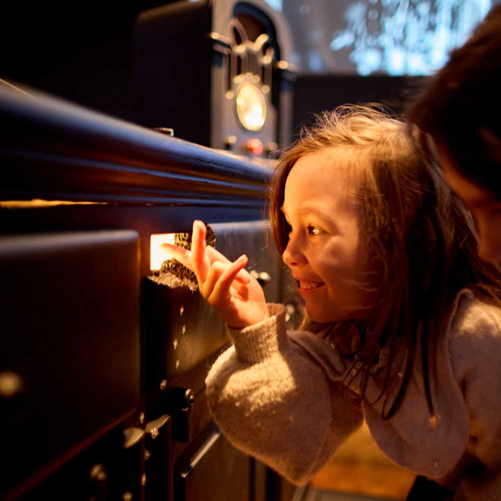 Two children crouch and look through a mouse hole with light coming out of it. Photograph.