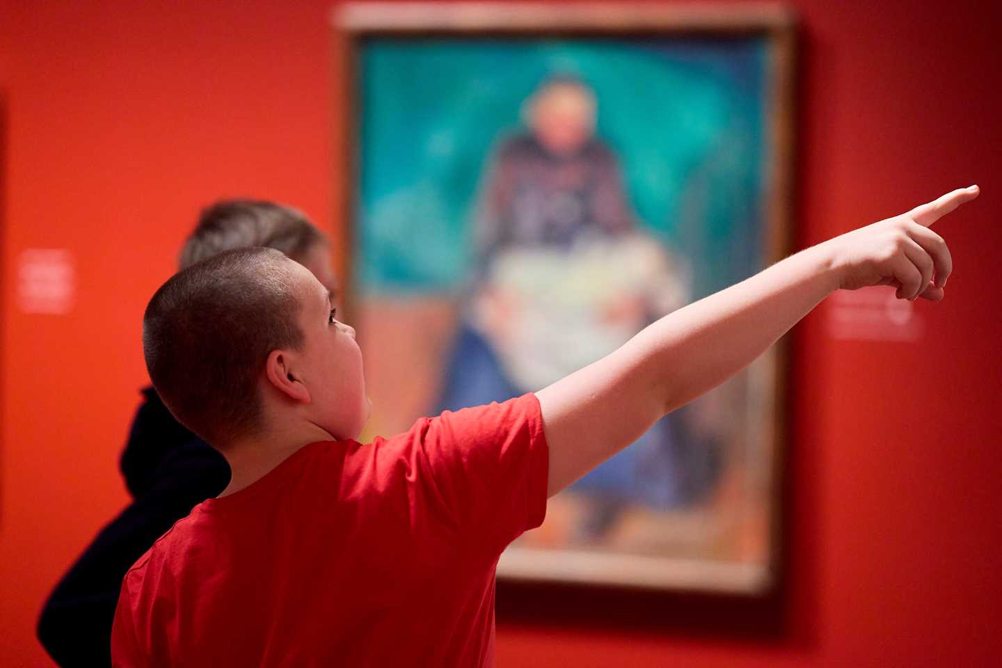 A young boy pointing at an artwork in the Infinite exhibition while talking to another boy. Photograph.