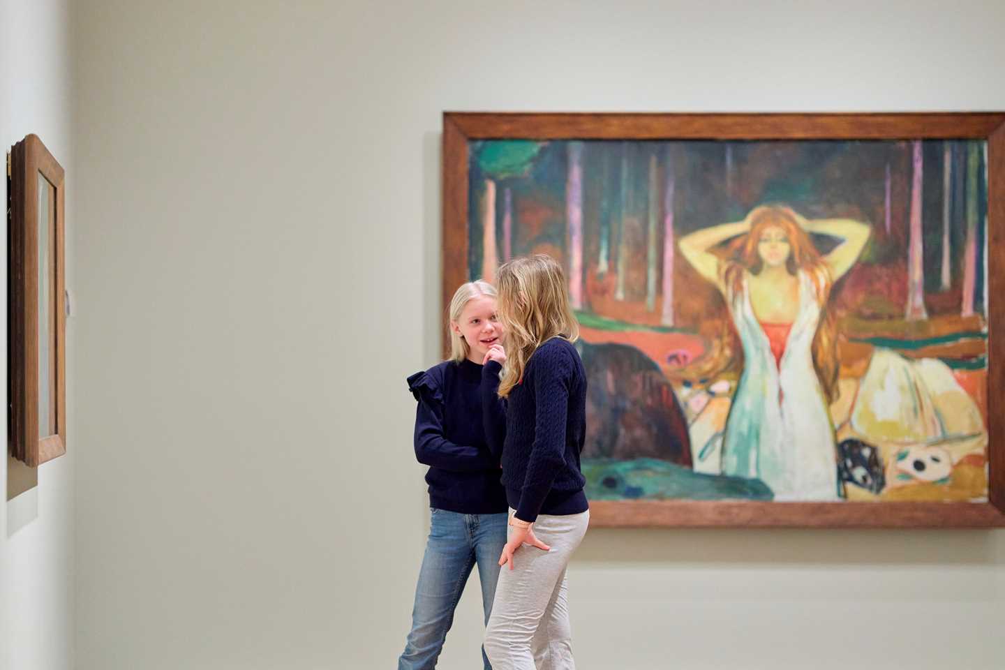 Two young girls talking surrounded by artworks in the Infinite exhibition. Photograph.