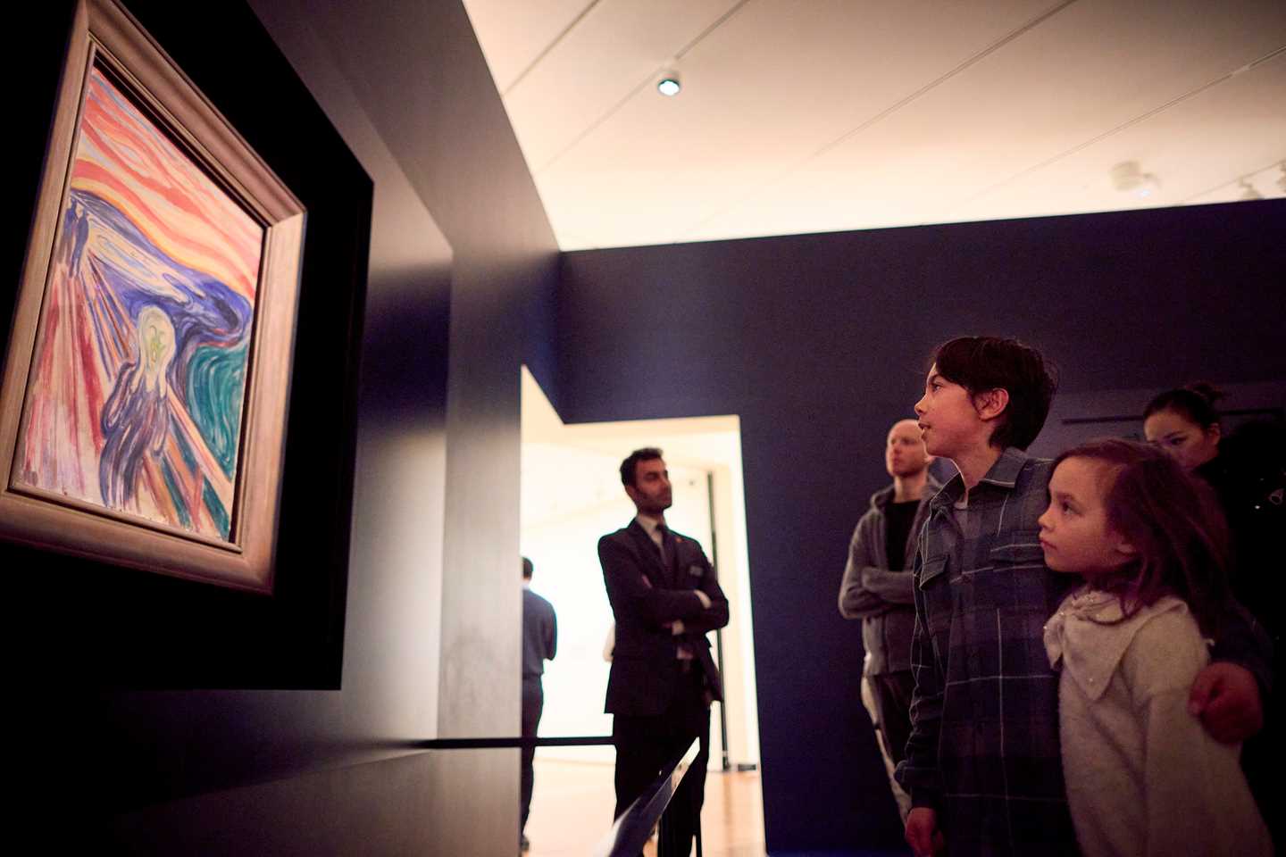 A family of four admiring The Scream by Edvard Munch, with a guard in the background. Photograph.