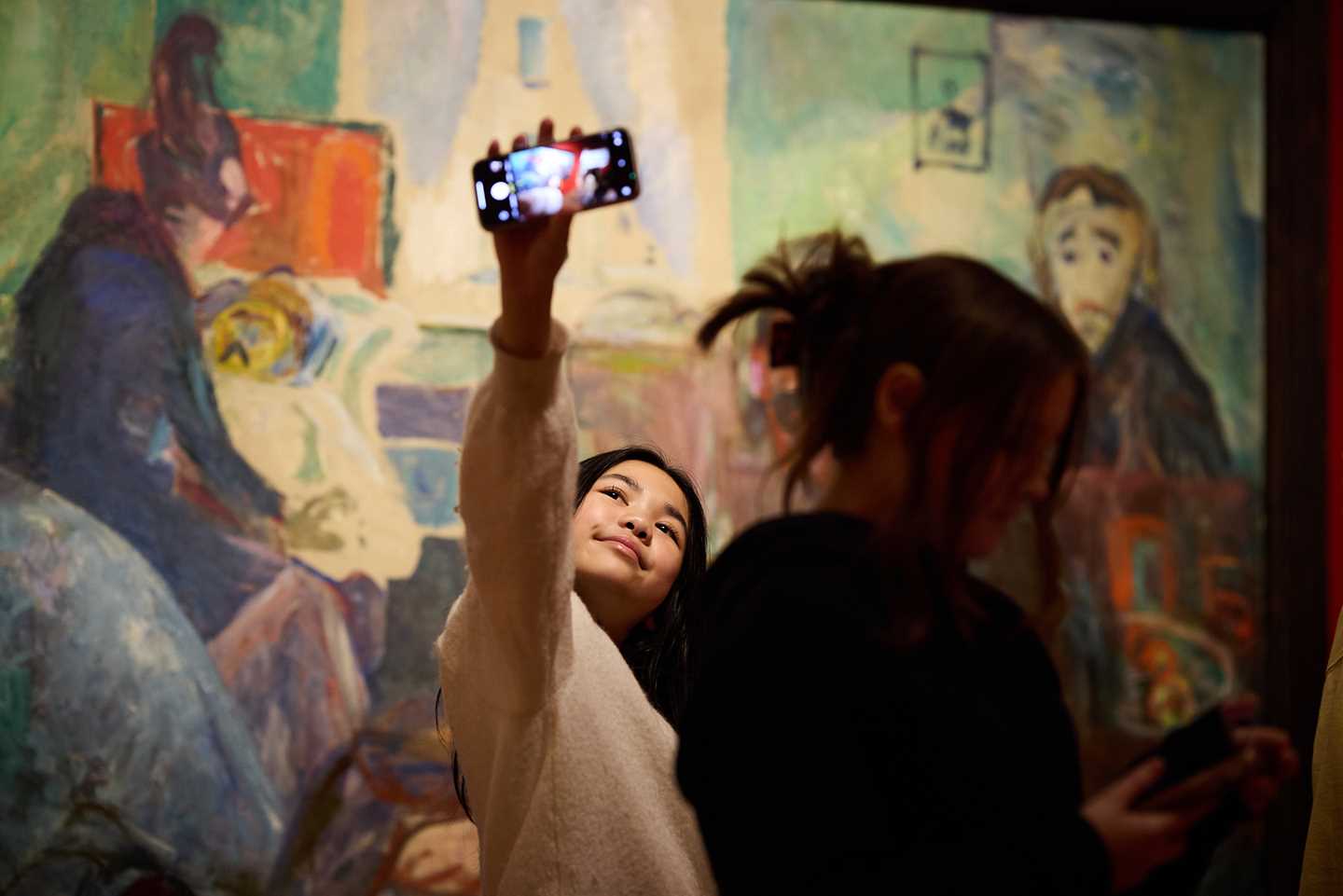 A young girl takes a photo of herself with her phone in front of a painting by Edvard Munch in the Infinite exhibition. Photograph.