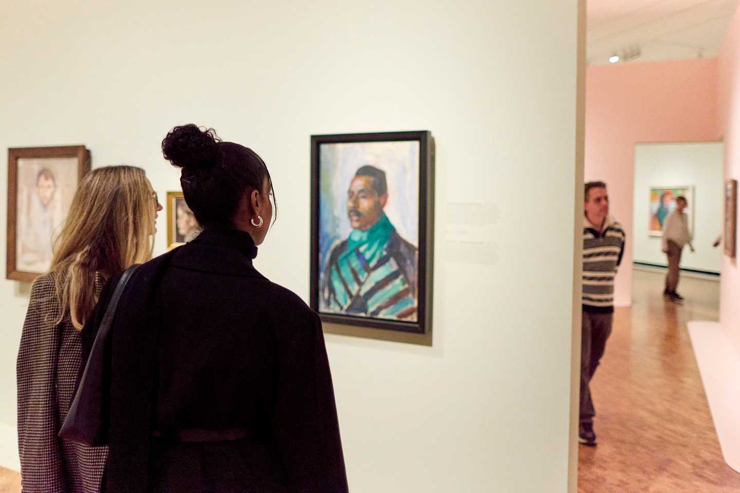 Two women with their backs to the camera looking at a portrait painting by Edvard Munch. Photograph.