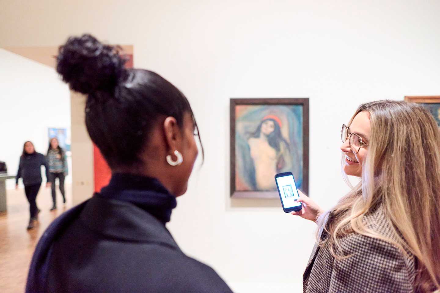Two women talking while looking at Madonna by Edvard Munch, one taking a photo with her phone. Photograph.