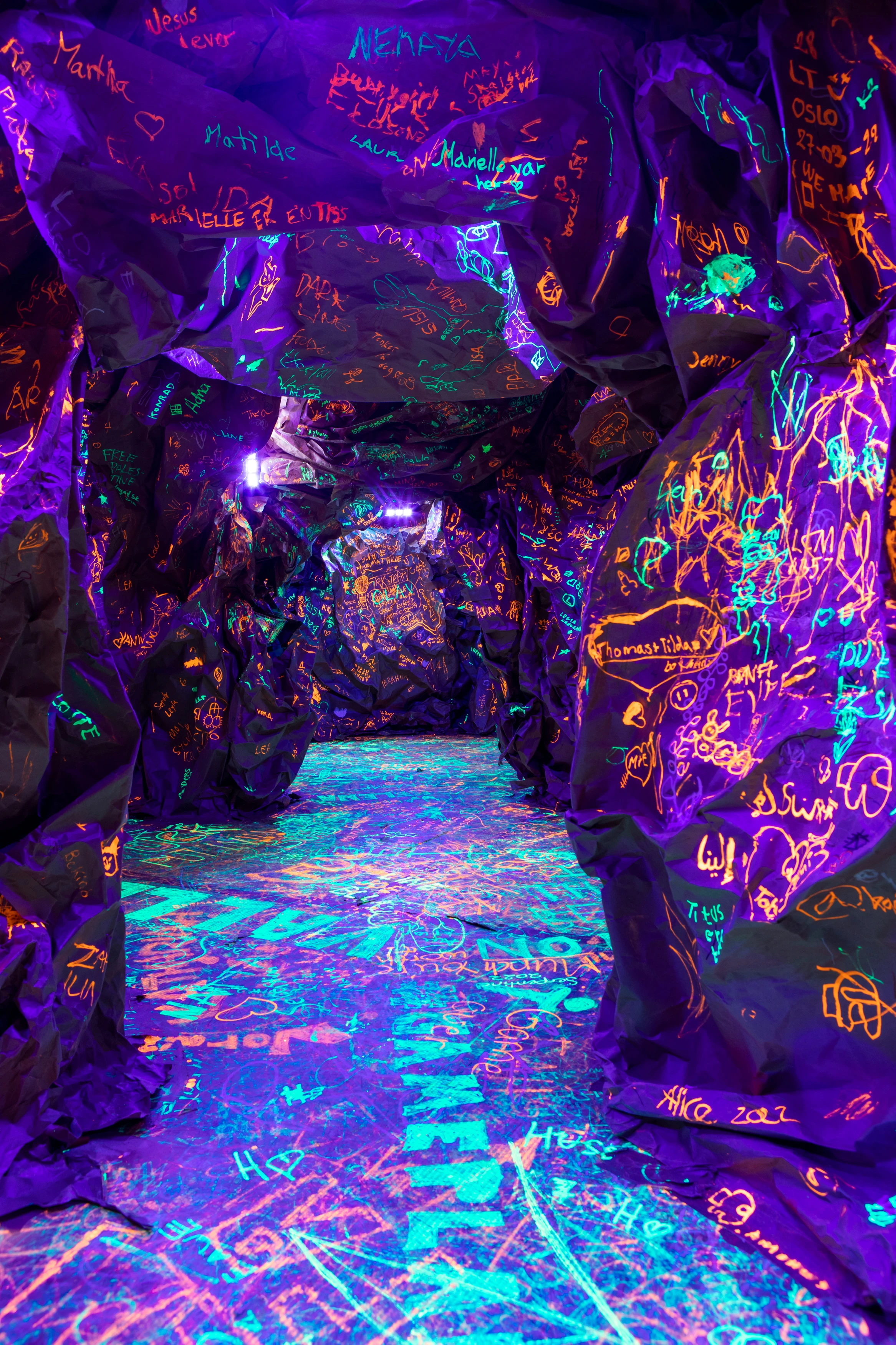 A knobbly, dark cave where children and adults have scribbled with glow-in-the-dark ink. Photograph.