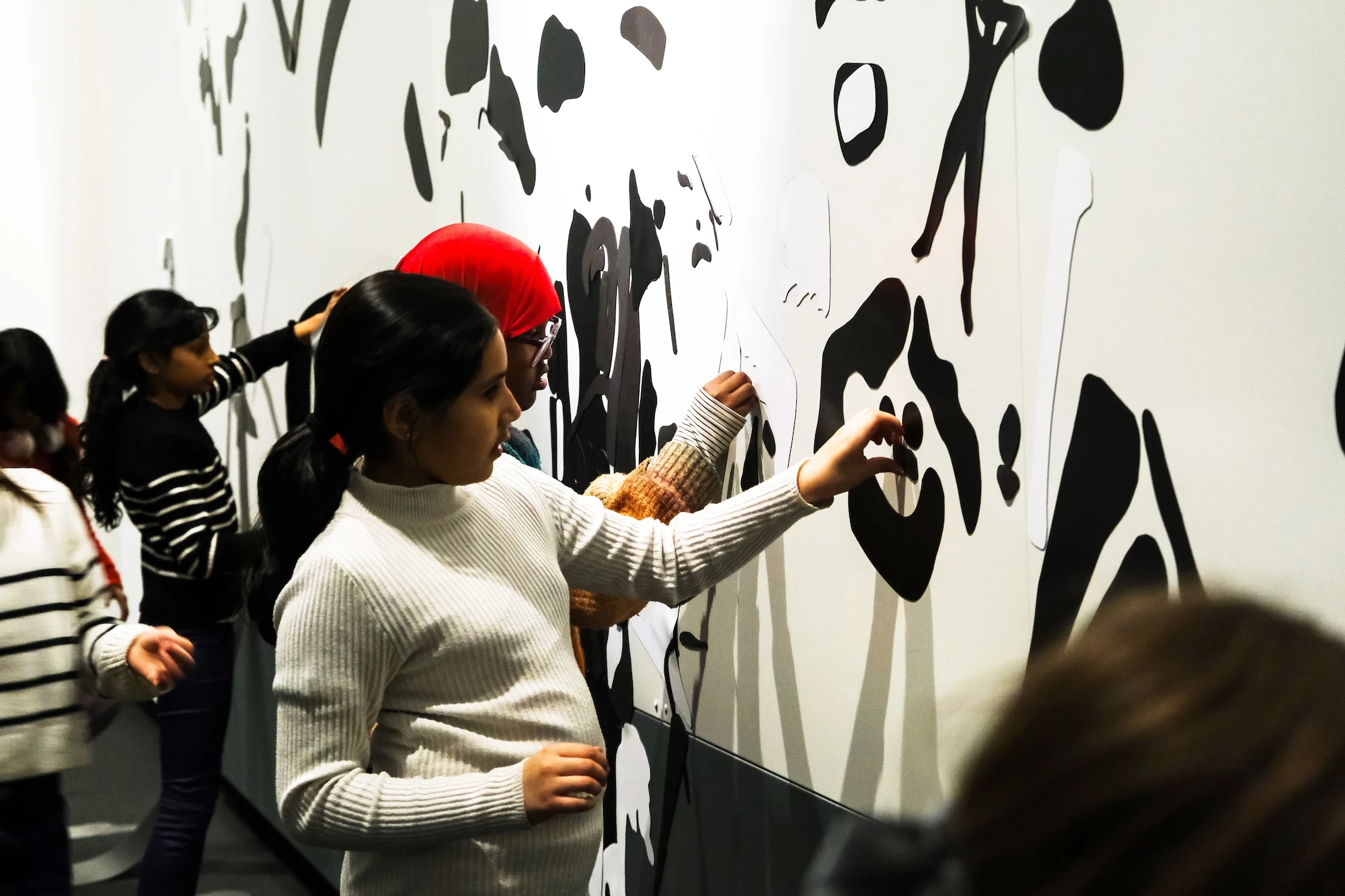 Four children attaching black magnets to a white wall. Photograph.