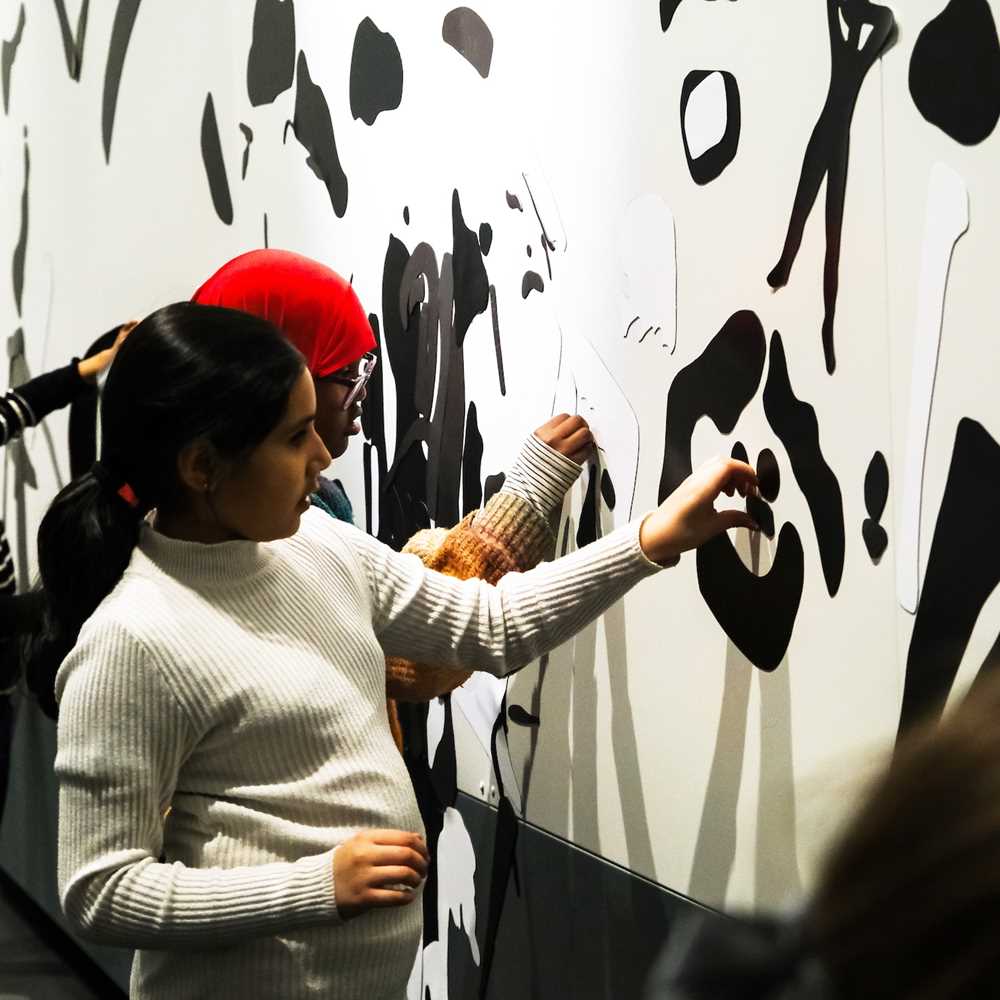 Four children attaching black magnets to a white wall. Photograph.