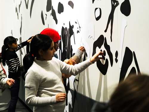 Four children attaching black magnets to a white wall. Photograph.