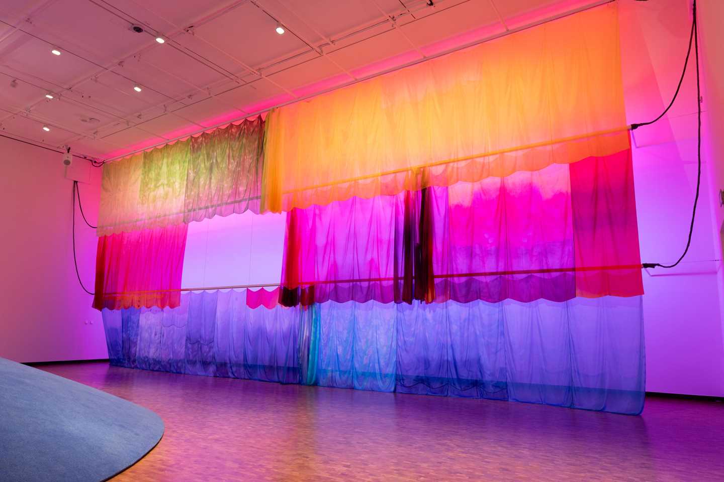 Colourful silk fabric hangs from tracks in the ceiling, moving to the music. Photograph.
