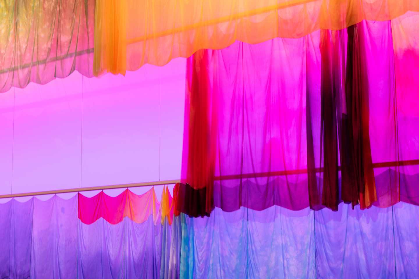 Colourful silk fabric hangs from tracks in the ceiling, moving to the music. Photograph.