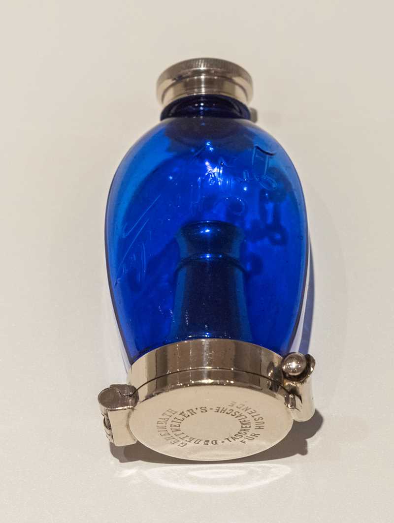 A cobalt blue, egg-shaped bottle for tuberculosis sufferers to spit into. Its length is 11 cm. The lid and metal base are made of metal.