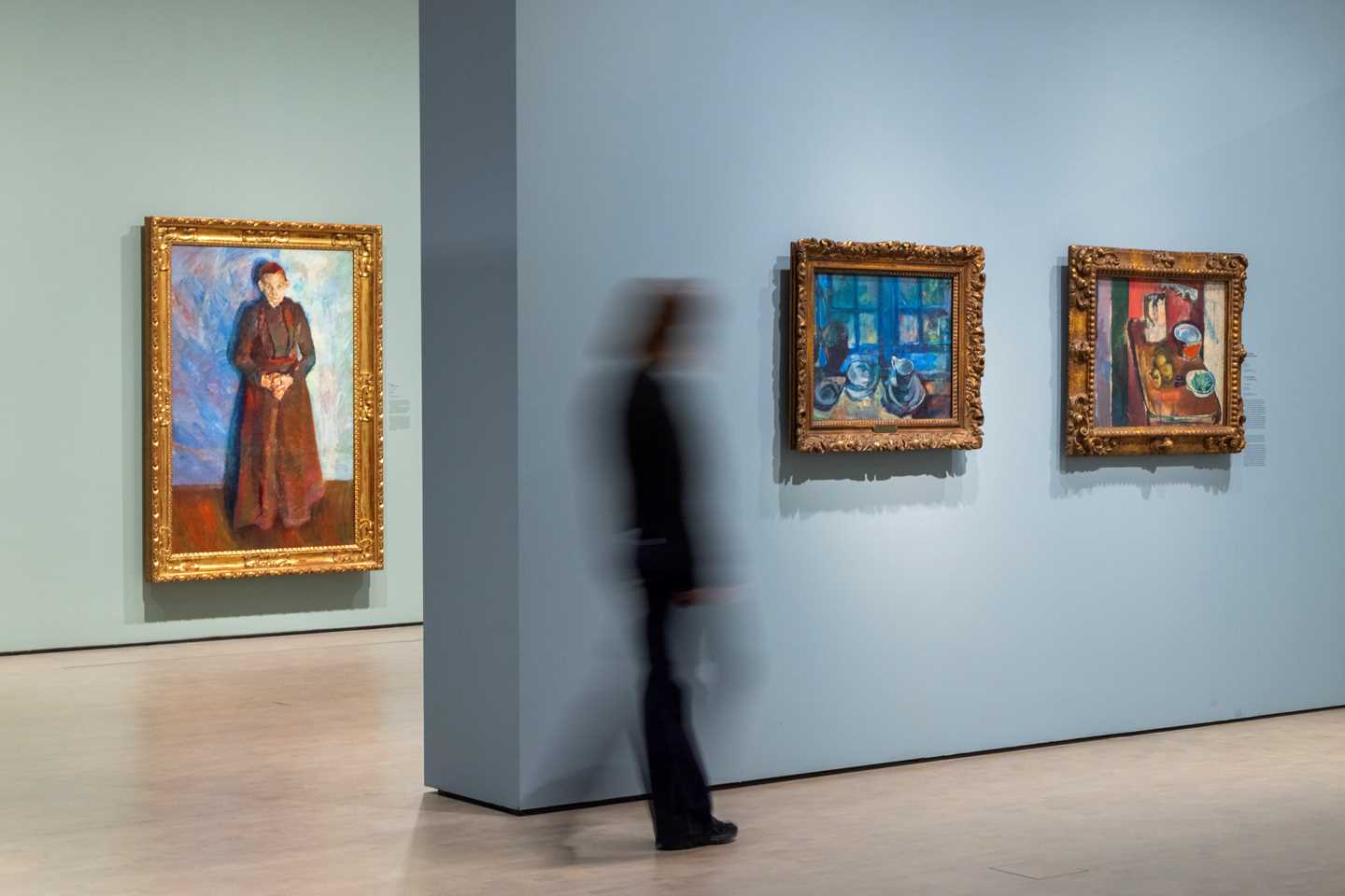 Image from an exhibition hall with a person walking toward the works The Blue Kitchen and The Red Kitchen by Ludvig Karsten. Photograph.