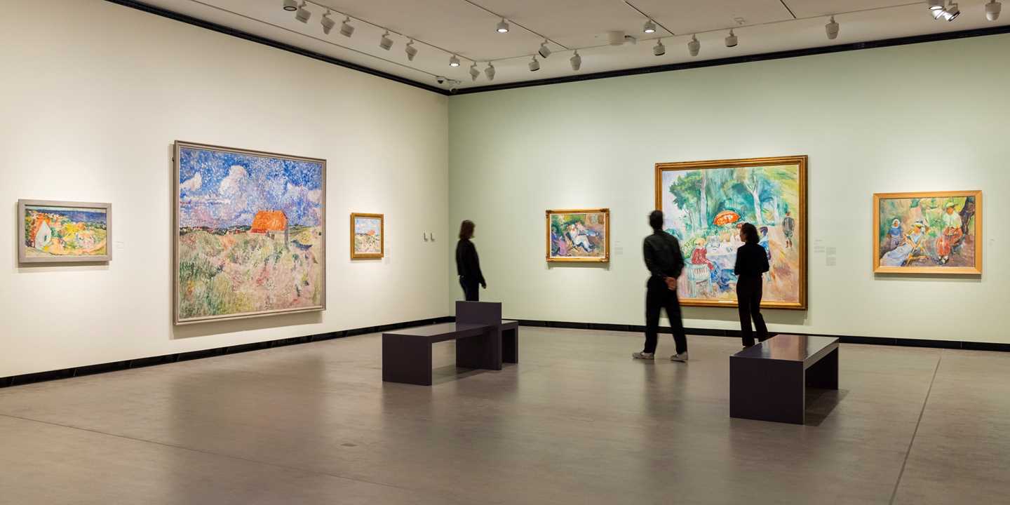 Three people standing in an exhibition hall looking at works by Ludvig Karsten. Photograph.