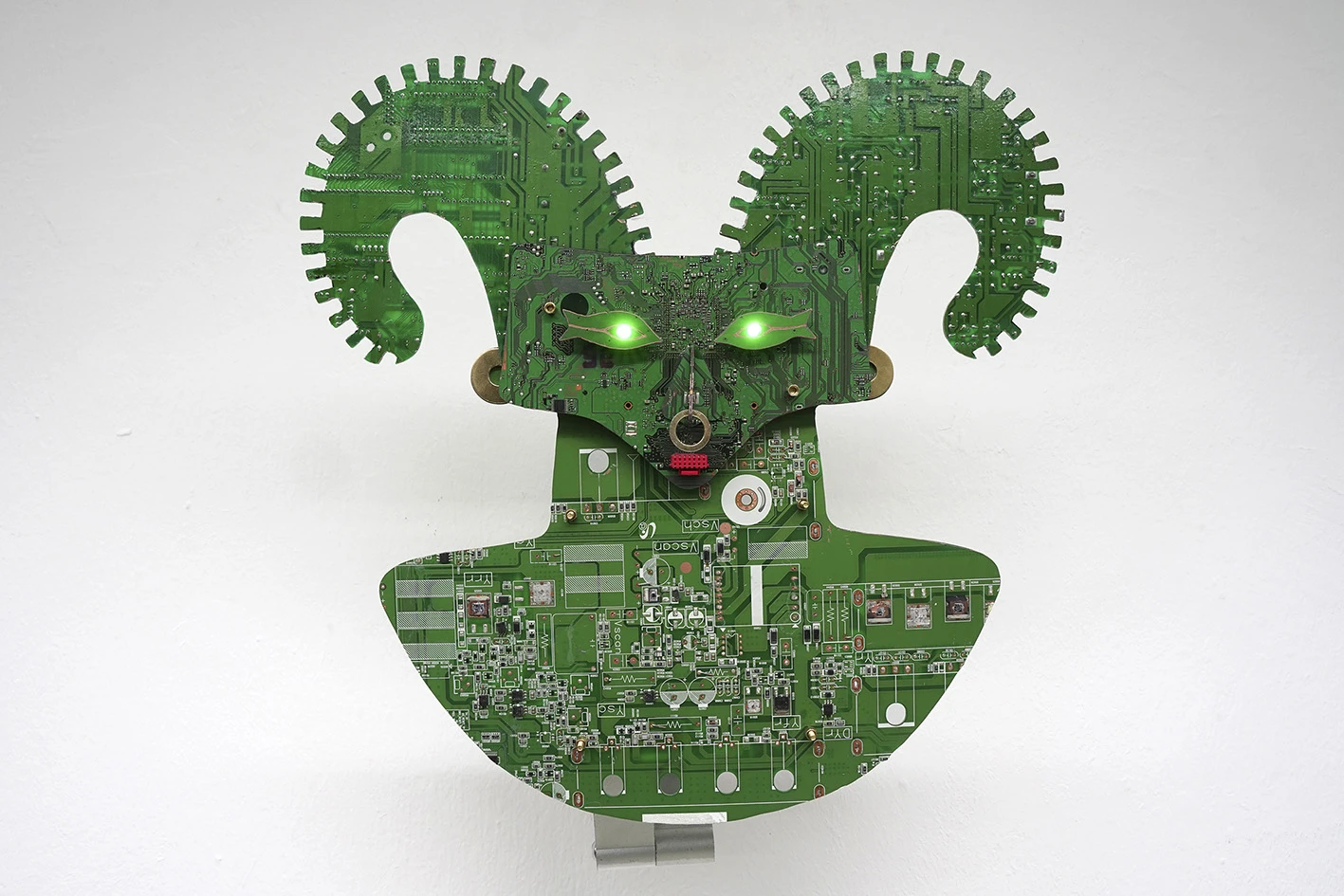 A two-dimensional green creature with horns and glowing green eyes, made from the inner parts of computers.