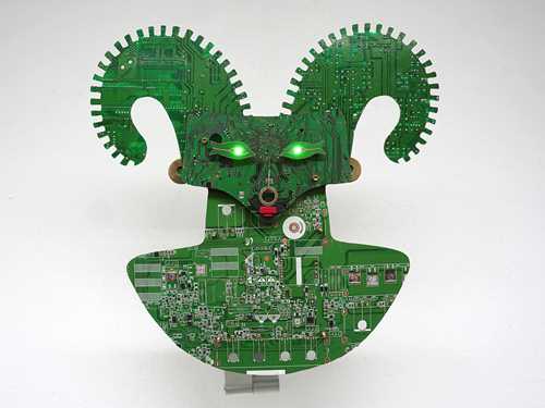 A two-dimensional green creature with horns and glowing green eyes, made from the inner parts of computers.