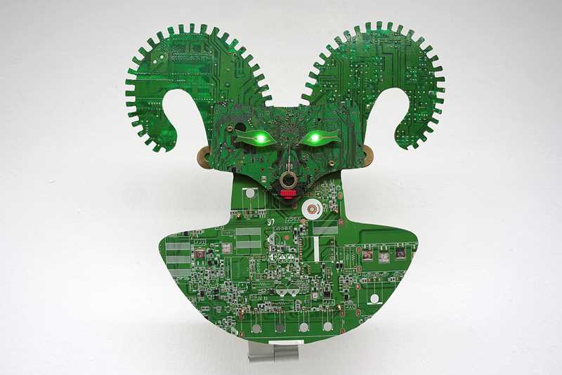 A two-dimensional green creature with horns and glowing green eyes, made from the inner parts of computers.