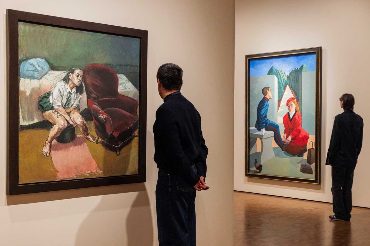 Two people stand with their backs to the camera, looking at two works by Paula Rego. Photograph.