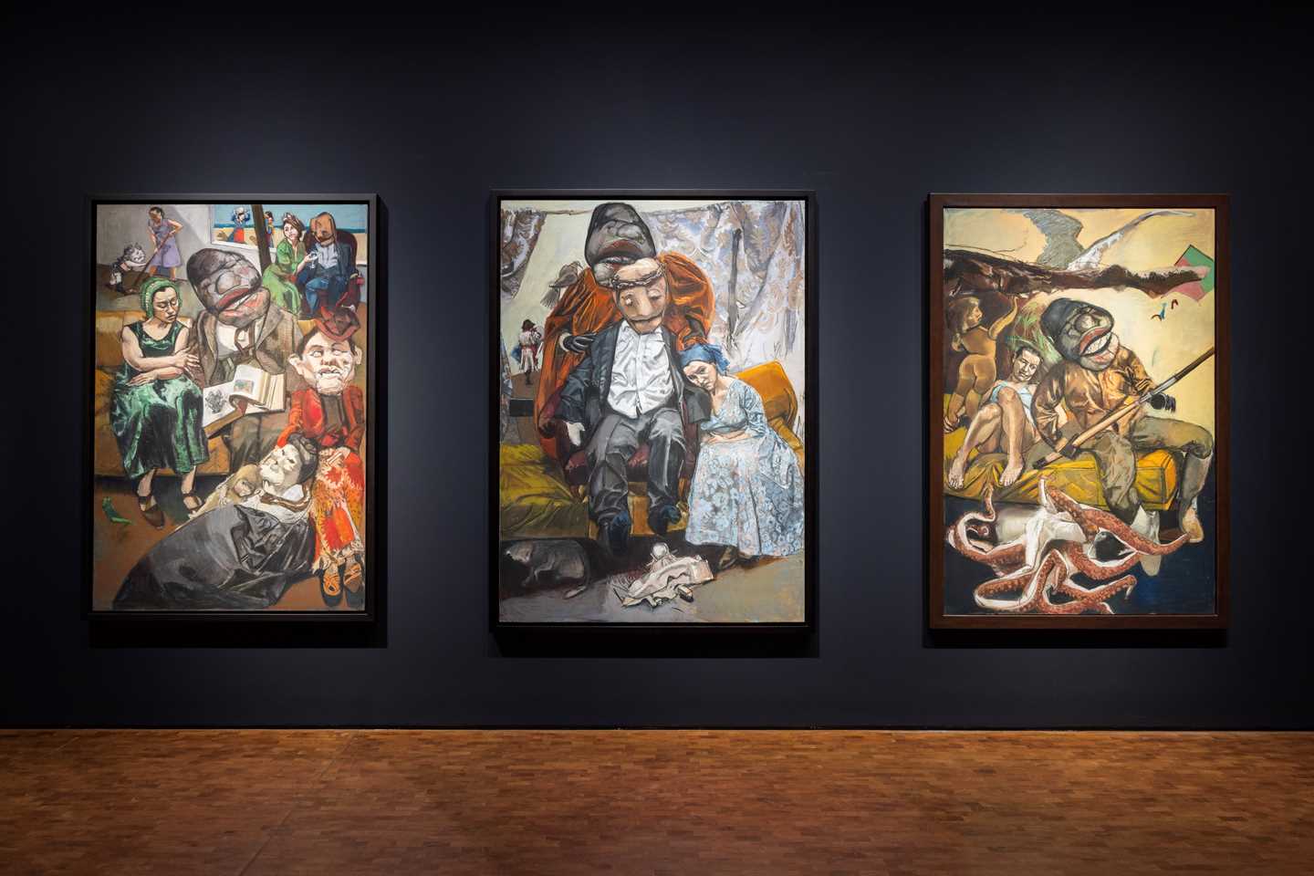 Three pastels by Paula Rego hang against a deep blue wall. Photograph.