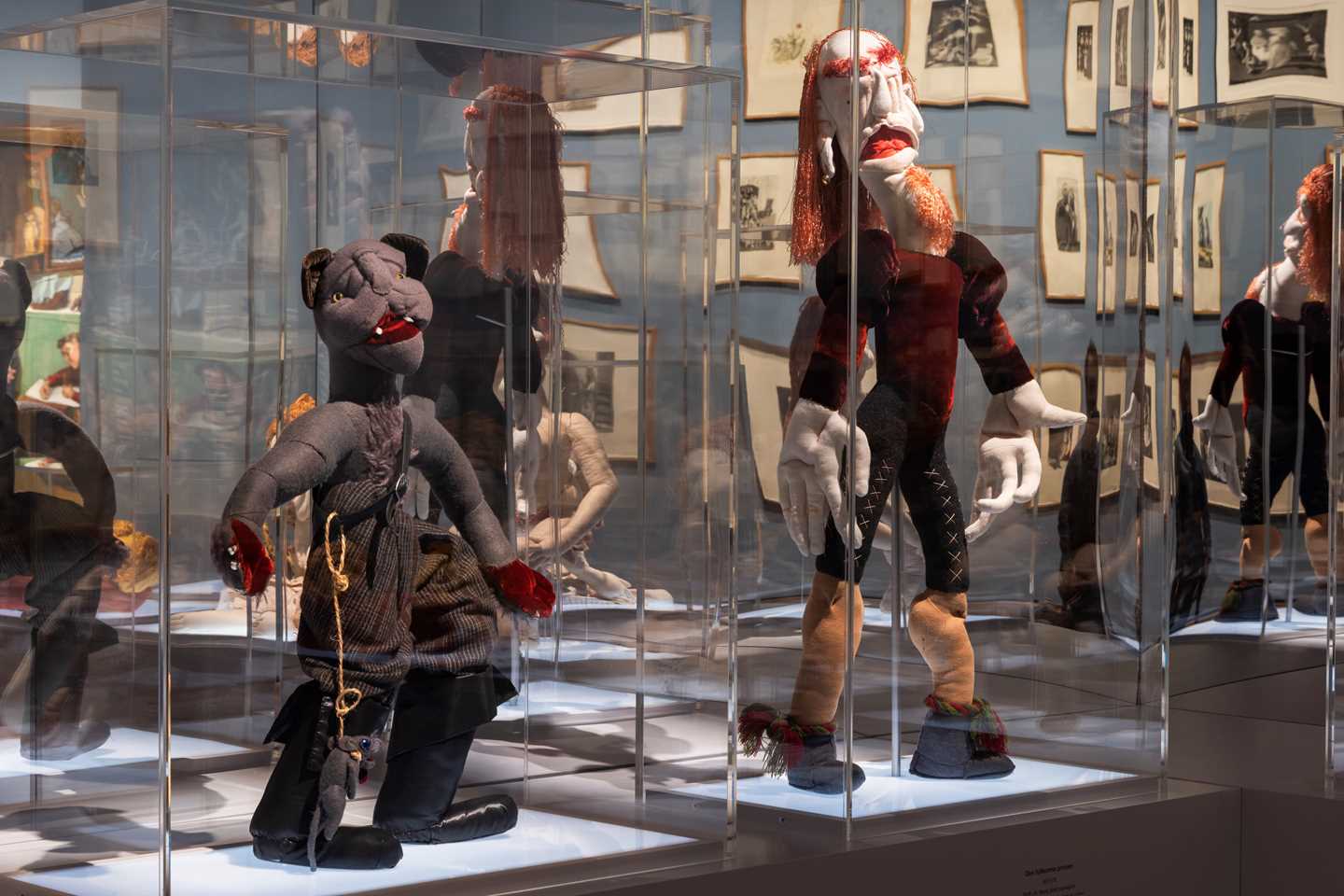 Two textile sculptures stand in separate glass display cases, each with a large mirror mounted behind them. Photograph.