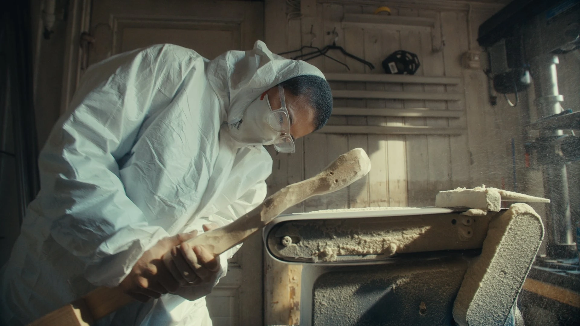 Artist Kim Hankyul in a full white coverall, mask and safety glasses, bent over sanding a log on an automatic sanding machine. Photograph.