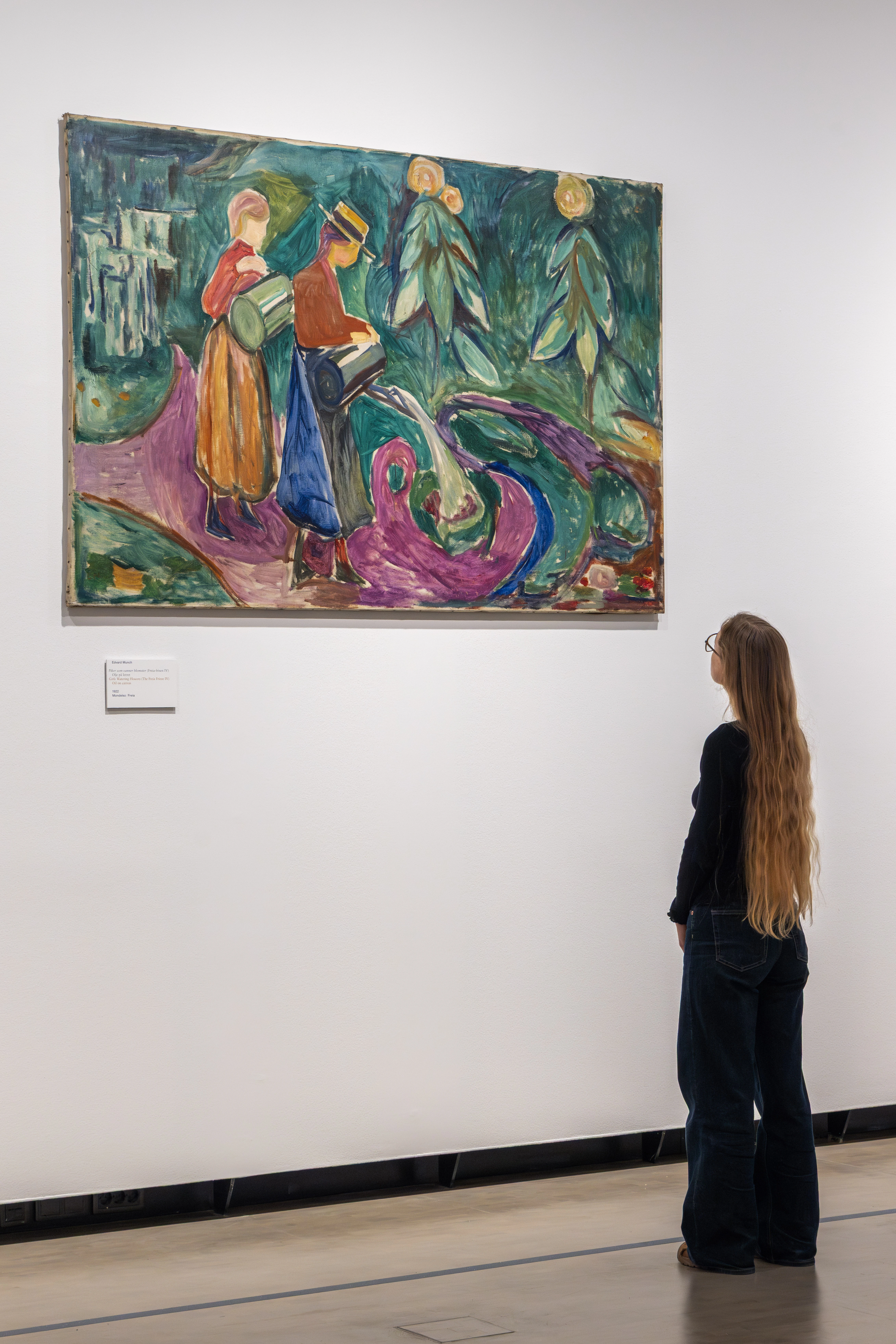 A woman with long hair looks at the work Girls Watering Flowers by Edvard Munch. Photograph.