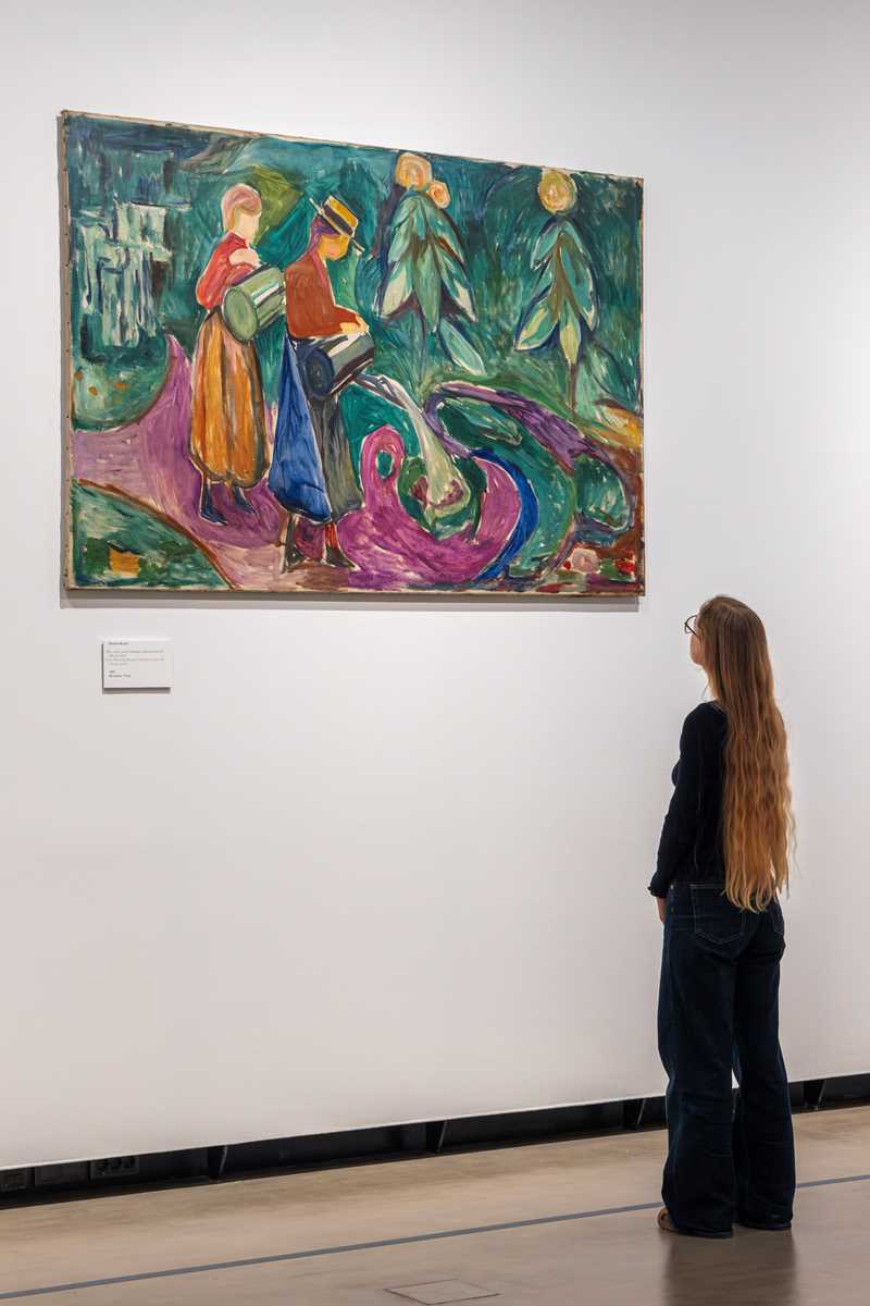 A woman with long hair looks at the work Girls Watering Flowers by Edvard Munch. Photograph.