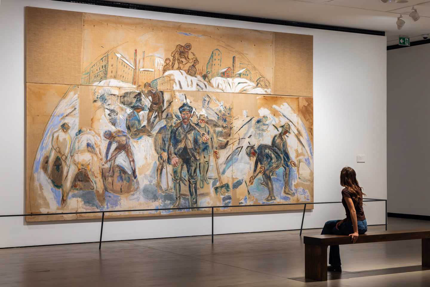 A woman sits on a bench, looking at a monumental painting by Edvard Munch. Photograph.