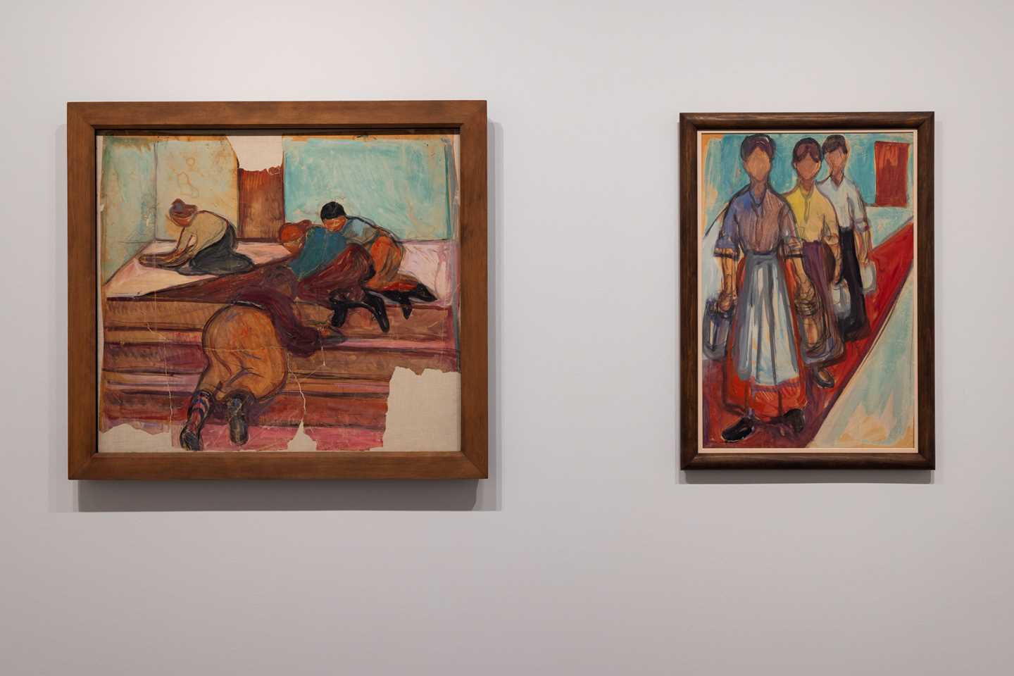 Two works by Edvard Munch hang on a white wall. Both are colourful works depicting women at labour. Photograph.