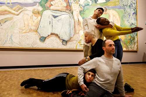 Five dancers in front of Edvard Munch's painting Alma Mater, performing Permanent Collection. They stand, sit, and lie intertwined with one another. Photograph.