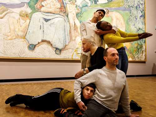 Five dancers in front of Edvard Munch's painting Alma Mater, performing Permanent Collection. They stand, sit, and lie intertwined with one another. Photograph.