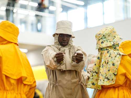 Four people in full rain gear and bucket hats perform a dance in the lobby at MUNCH.